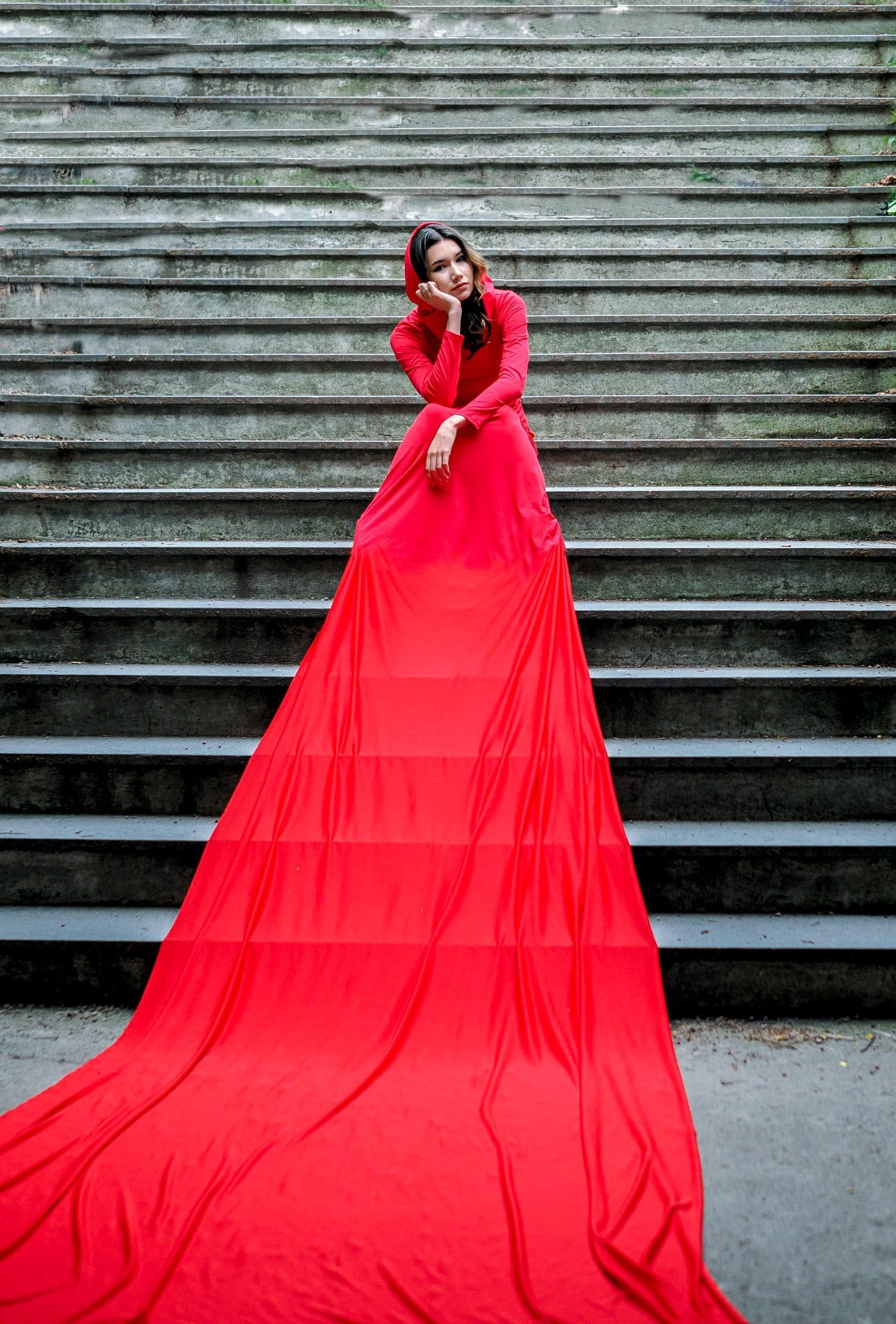 A woman in a red dress sits gracefully on a set of stairs, exuding elegance and poise.